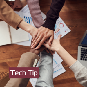 December Tech Tip. Photo of people near wooden table. Colleagues holding hands in unity.